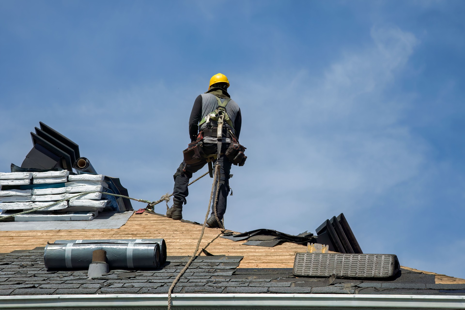Professional Roofer with Hard Hat and Nailer Installing Shingles on Residential Roof