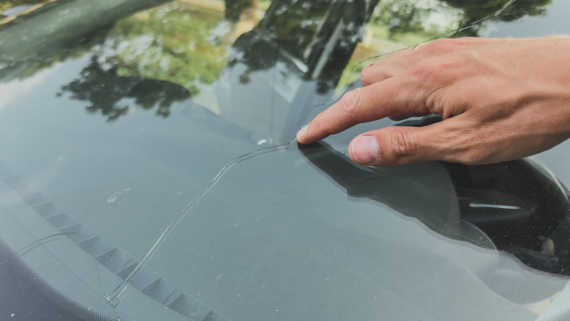Close-up of a hand pointing at a long crack in a car windshield, highlighting glass damage and need for repair or replacement, vehicle maintenance concept