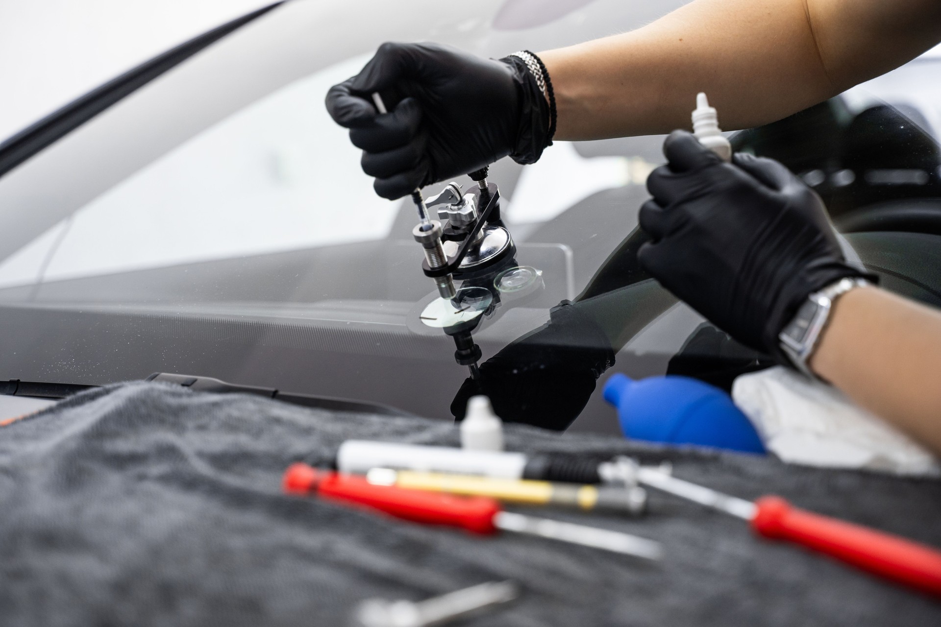 Resin repair on windshield using injector application to restore structural clarity. Windshield crack repair using resin injection. Technician using windshield injector tool to fix bullseye crack.